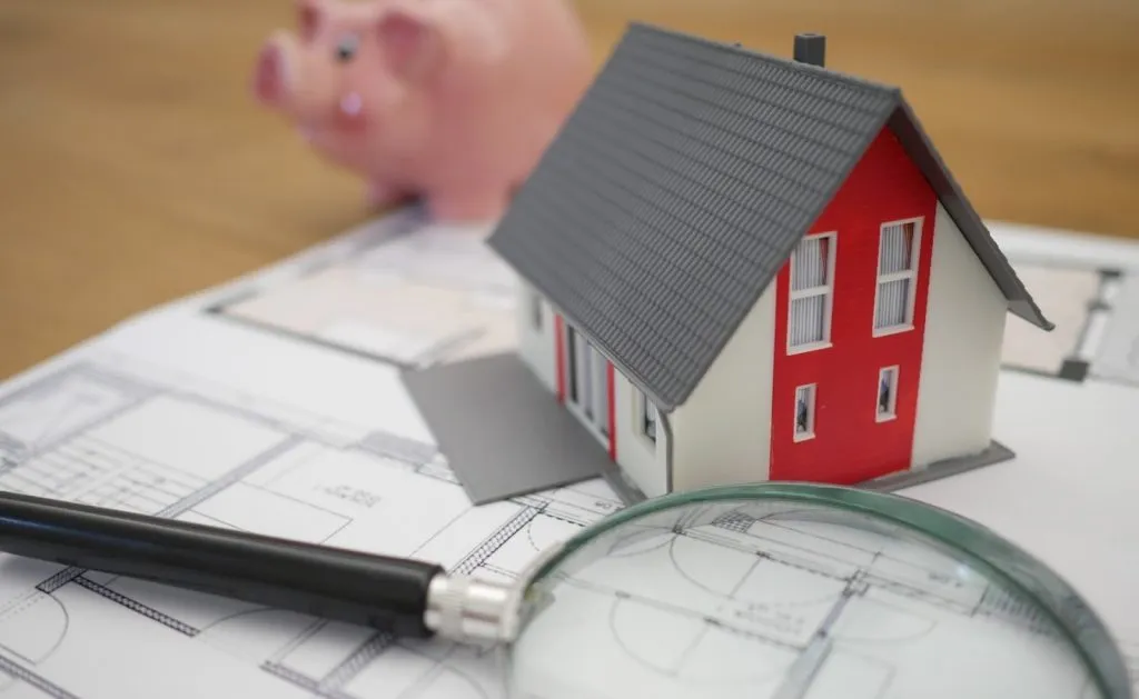 Model house, magnifying glass and piggy bank on top of floor plans