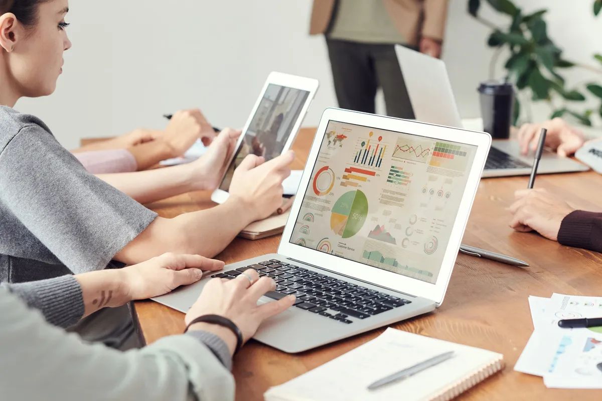 Team meeting around a table with laptops showing marketing dashboards
