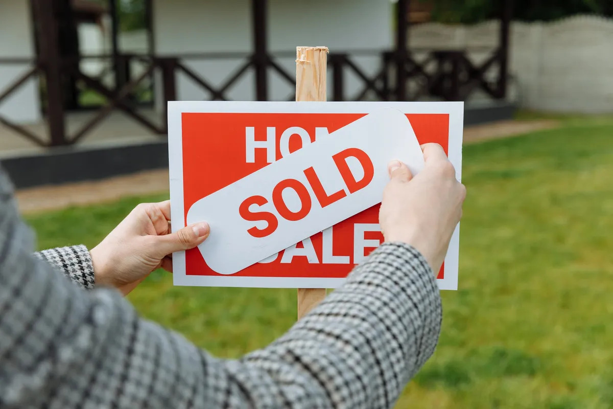 A realtor placing a sold sticker on a property sign