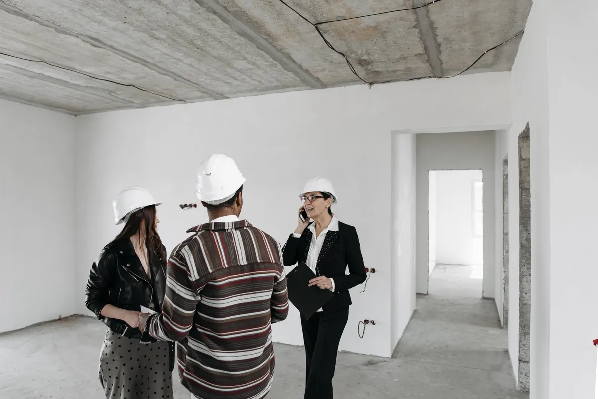 An agent with a clipboard walking two clients through an unfinished home in hard hats