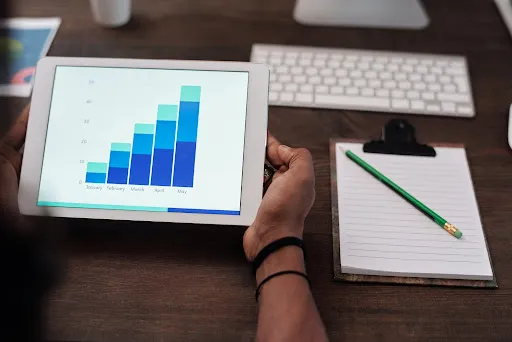 Hands holding a tablet showing a rising bar chart over a desk