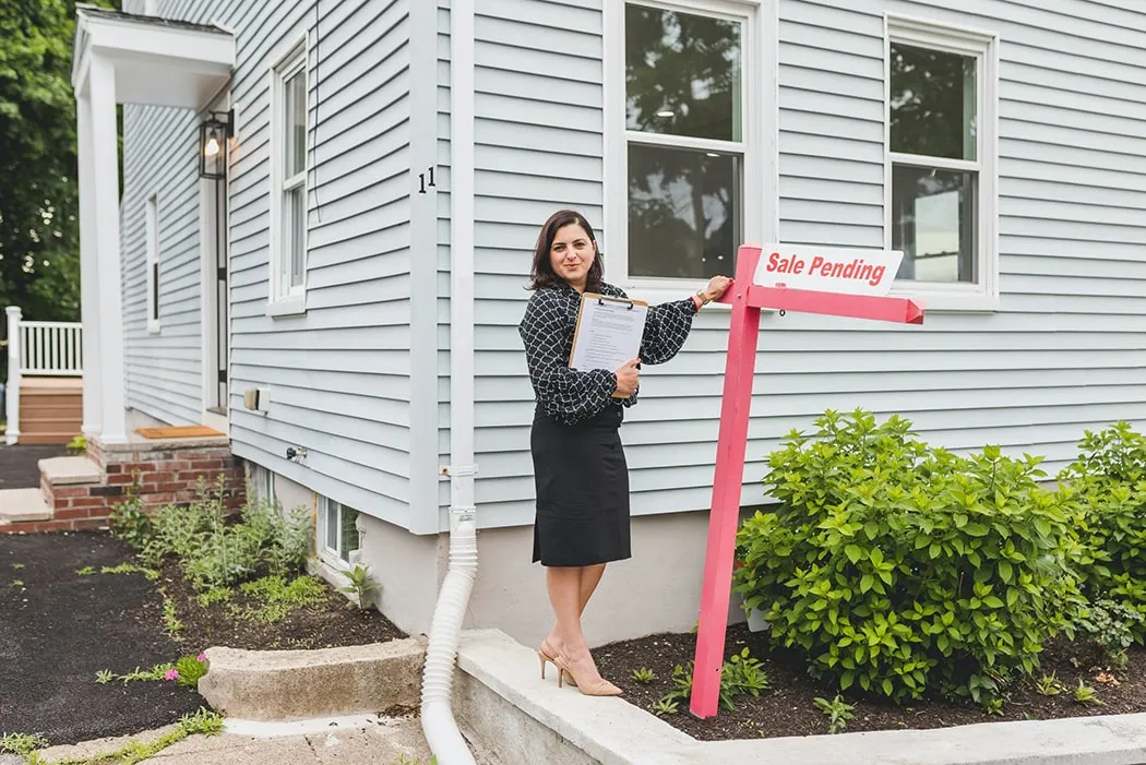 A real estate agent with a clipboard beside a sale pending sign