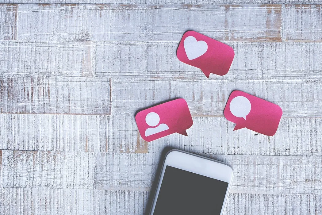 Pink social media icons for likes, followers and comments beside a smartphone