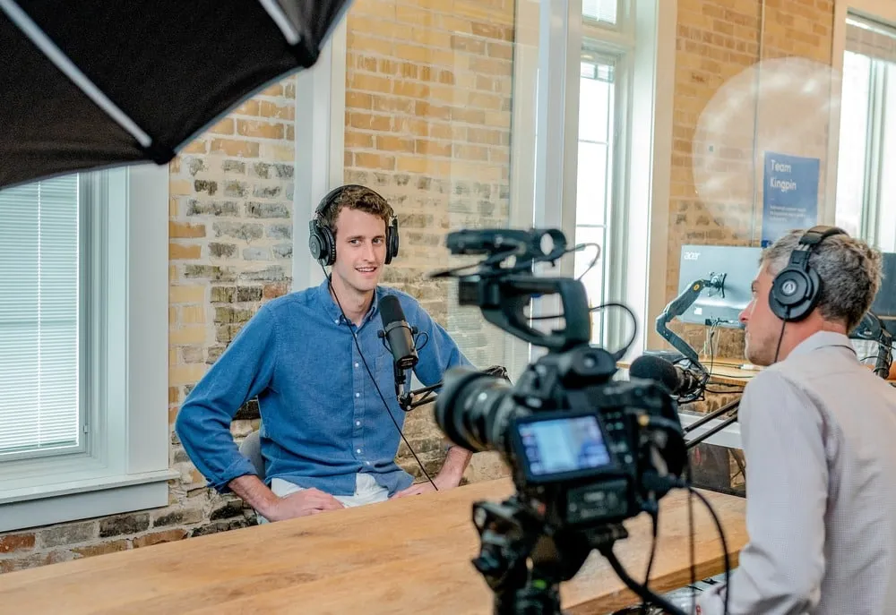 A podcast interview being recorded on camera in a studio with brick walls