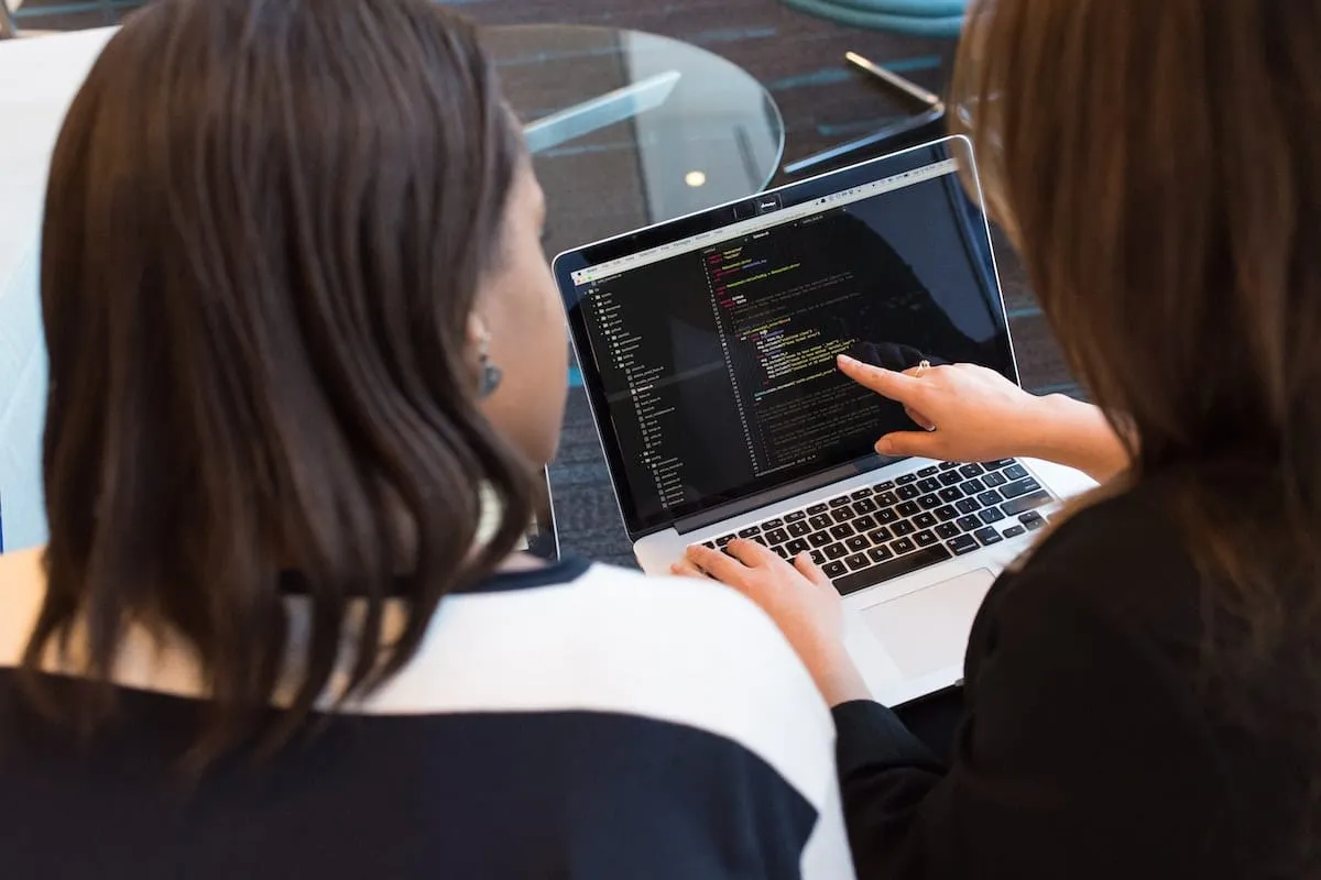 Two colleagues looking at code on a laptop screen together