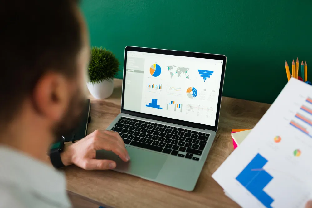 Rear view of a young man working on his laptop and looking at a work report and graphs