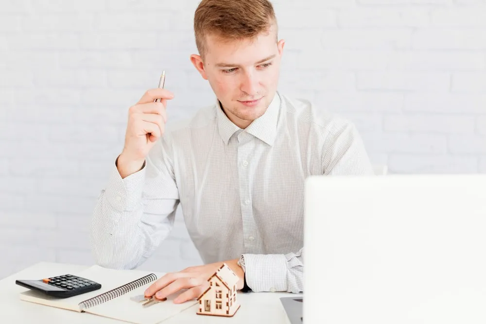 Agent at a desk with a laptop, notebook, calculator and a small model house