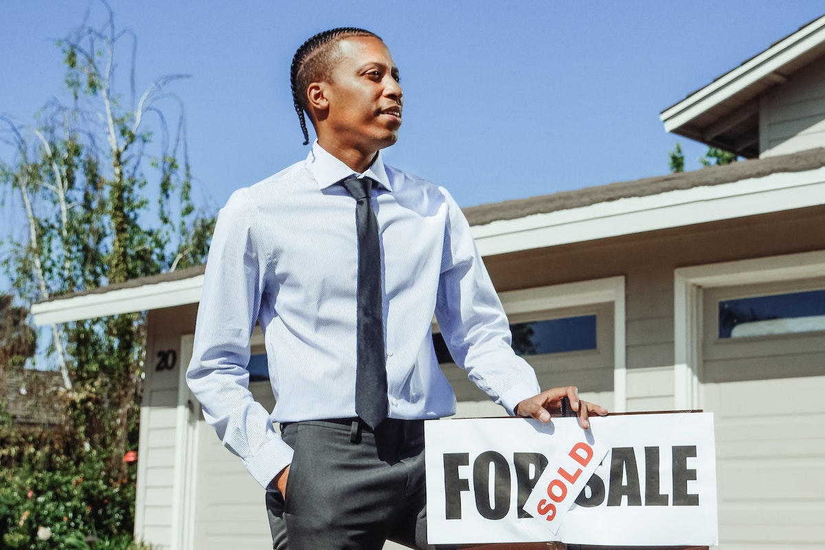 Man in Dress Shirt and Black Necktie Holding on a Sold Sign